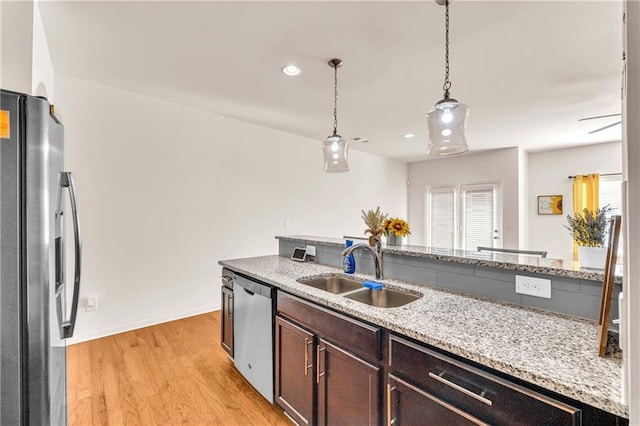 kitchen featuring appliances with stainless steel finishes, decorative light fixtures, light wood-type flooring, light stone counters, and sink