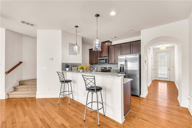 kitchen featuring decorative light fixtures, kitchen peninsula, appliances with stainless steel finishes, a breakfast bar area, and dark brown cabinets