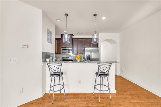 kitchen featuring kitchen peninsula, appliances with stainless steel finishes, dark brown cabinets, pendant lighting, and a breakfast bar