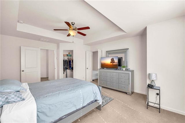 bedroom featuring a spacious closet, a tray ceiling, a closet, and ceiling fan