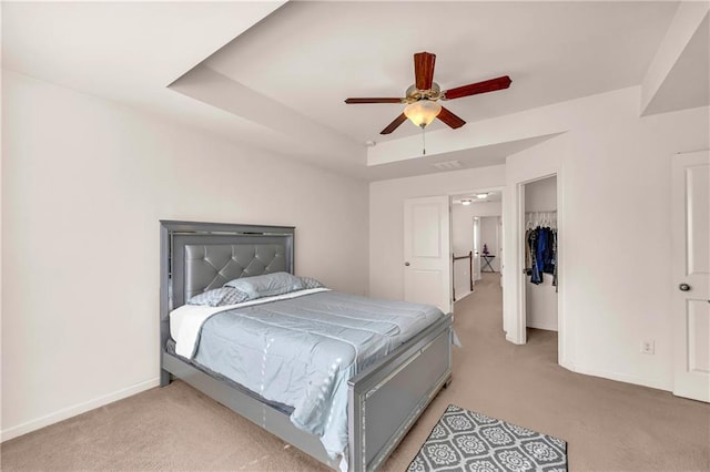 bedroom featuring ceiling fan, a closet, light carpet, and a raised ceiling