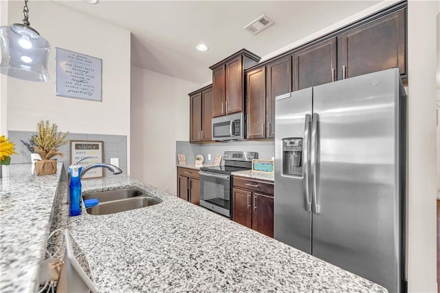 kitchen with appliances with stainless steel finishes, hanging light fixtures, light stone counters, dark brown cabinetry, and sink