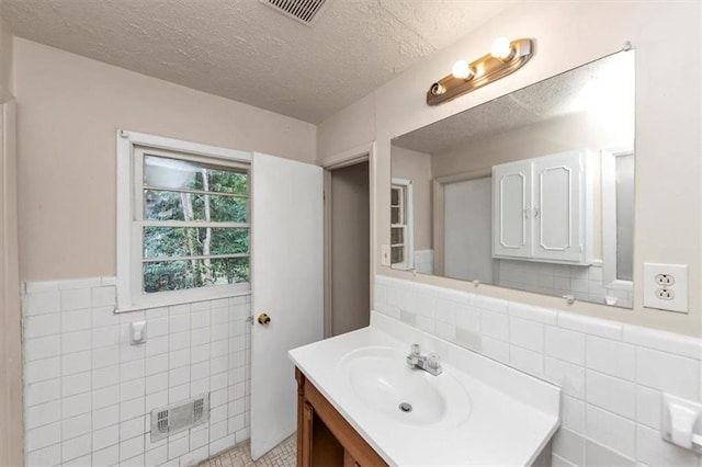 bathroom featuring a wainscoted wall, tile walls, visible vents, vanity, and a textured ceiling