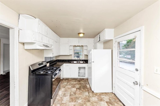 kitchen featuring dark countertops, gas stove, freestanding refrigerator, white cabinetry, and a sink