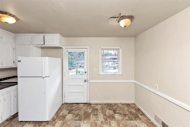 kitchen featuring baseboards, dark countertops, stone finish floor, freestanding refrigerator, and white cabinetry