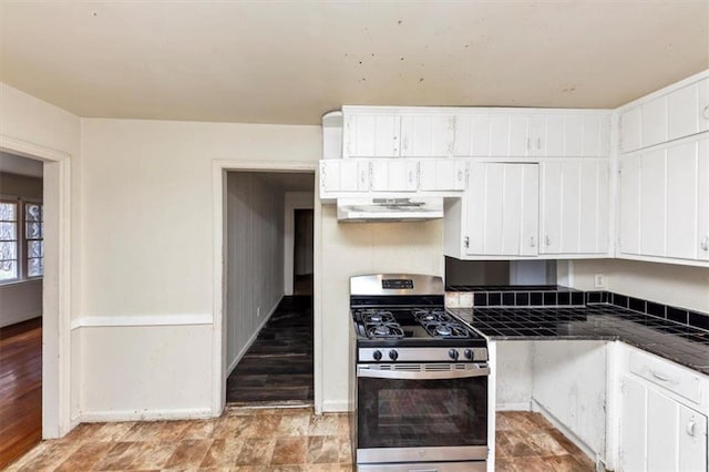 kitchen with stainless steel gas range oven, extractor fan, white cabinetry, and baseboards