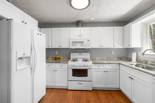 kitchen with white appliances, white cabinets, wood finished floors, and a sink