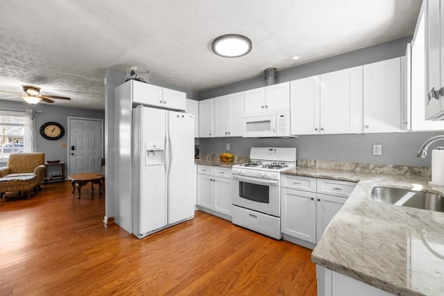 kitchen with a sink, white appliances, light wood-style floors, and white cabinets