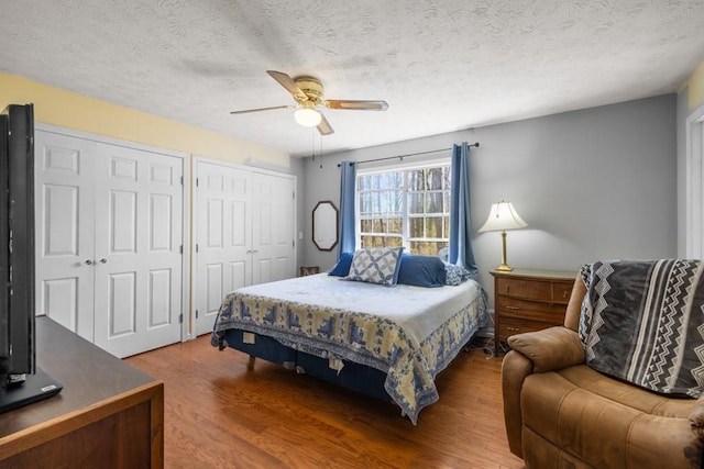 bedroom featuring a textured ceiling, two closets, ceiling fan, and wood finished floors