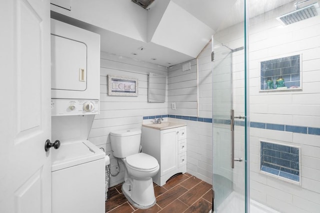 full bathroom featuring vanity, wood finish floors, a stall shower, stacked washer and clothes dryer, and toilet