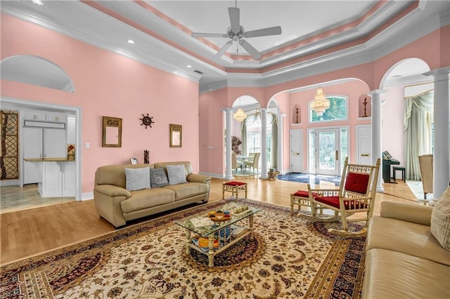 living area featuring ornate columns, a towering ceiling, crown molding, ceiling fan, and arched walkways