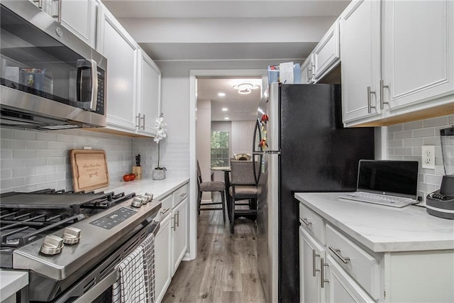 2376 Wellington Cir, Lithonia, GA 30058 - kitchen with appliances with stainless steel finishes, light wood-style flooring, backsplash, and white cabinetry