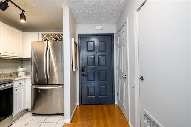 kitchen featuring appliances with stainless steel finishes, a textured ceiling, light hardwood / wood-style floors, white cabinets, and tasteful backsplash