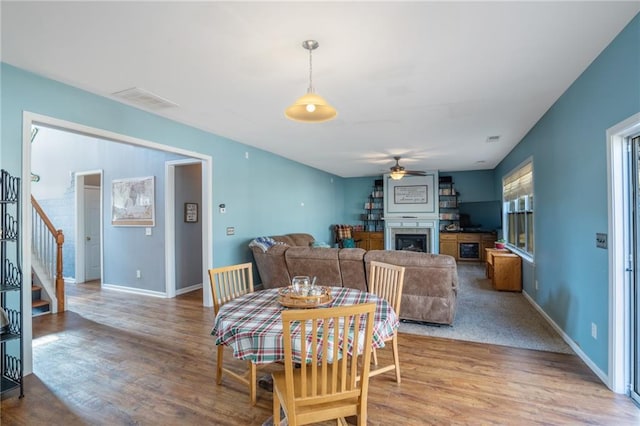 dining area featuring a fireplace, stairway, a ceiling fan, wood finished floors, and baseboards