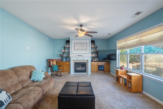 living area with visible vents, a glass covered fireplace, light carpet, ceiling fan, and baseboards