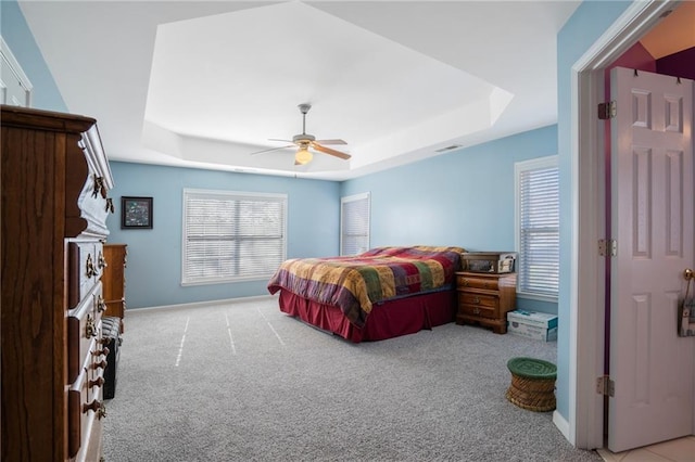 bedroom featuring light carpet, visible vents, a raised ceiling, and a ceiling fan