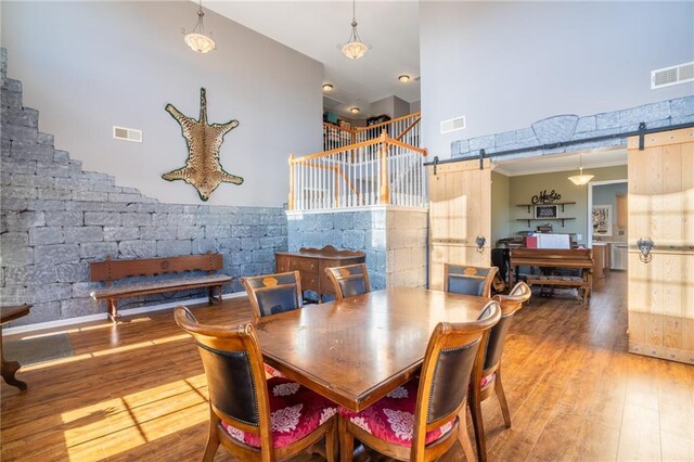 dining area featuring wood finished floors, visible vents, a towering ceiling, and a barn door