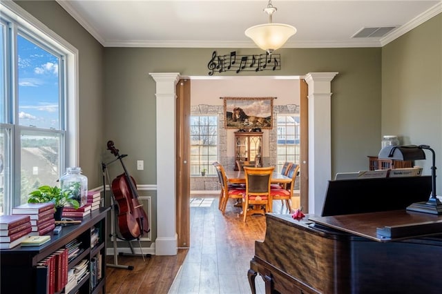 home office with a healthy amount of sunlight, visible vents, ornate columns, and wood finished floors