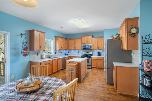 kitchen with light countertops, appliances with stainless steel finishes, a kitchen island, a sink, and light wood-type flooring