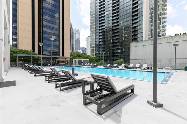 community pool with a view of city, a patio area, and fence