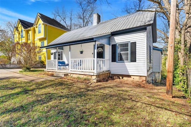 view of front of house with metal roof, a front yard, a porch, and a chimney