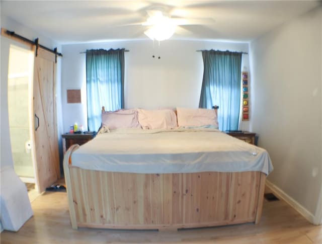 bedroom featuring ceiling fan, a barn door, and light hardwood / wood-style flooring