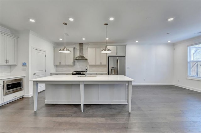 kitchen featuring sink, wall chimney range hood, pendant lighting, a kitchen island with sink, and appliances with stainless steel finishes