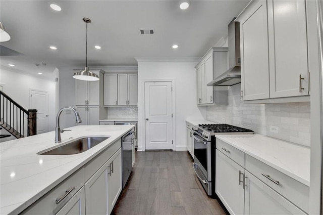 kitchen featuring hanging light fixtures, sink, wall chimney exhaust hood, appliances with stainless steel finishes, and light stone counters