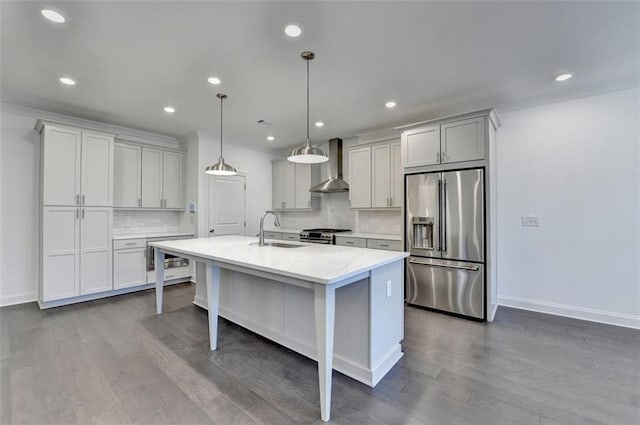 kitchen with sink, a kitchen island with sink, stainless steel appliances, wall chimney range hood, and decorative backsplash