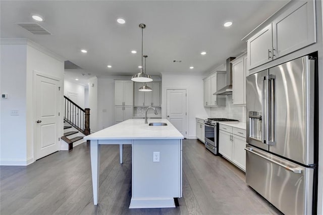 kitchen with pendant lighting, a kitchen island with sink, wall chimney range hood, sink, and stainless steel appliances