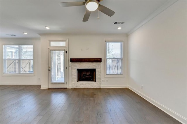 unfurnished living room with dark wood-type flooring, a stone fireplace, ceiling fan, and ornamental molding