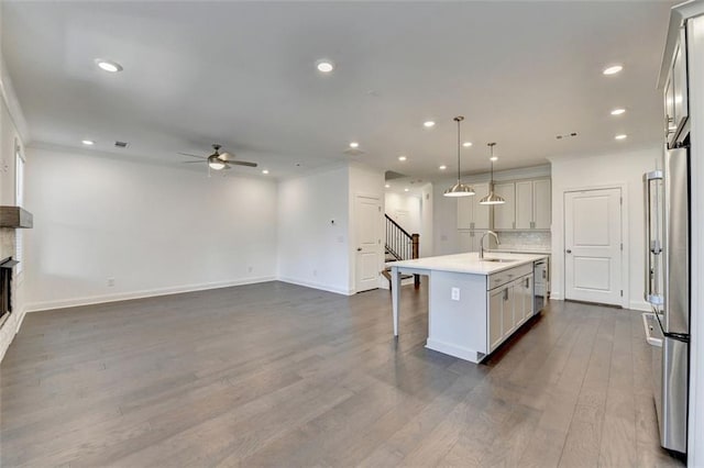 kitchen with ceiling fan, dark hardwood / wood-style floors, backsplash, pendant lighting, and a kitchen island with sink