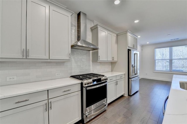 kitchen with wall chimney exhaust hood, wood-type flooring, white cabinetry, and appliances with stainless steel finishes