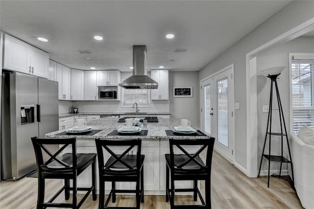 kitchen featuring stainless steel appliances, island exhaust hood, light stone countertops, and white cabinets