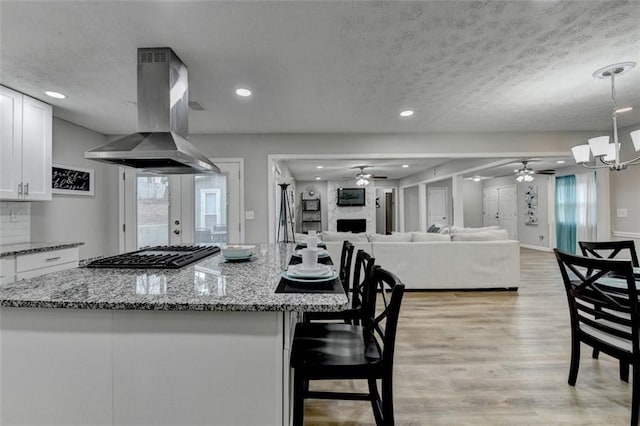 kitchen featuring white cabinetry, island exhaust hood, light stone countertops, and stainless steel gas cooktop