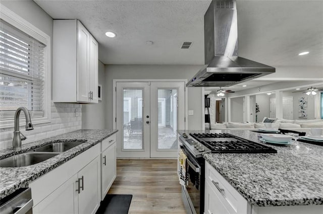 kitchen with french doors, sink, appliances with stainless steel finishes, island exhaust hood, and white cabinets