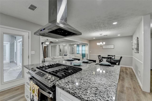 kitchen featuring pendant lighting, island range hood, stainless steel stove, white cabinetry, and light hardwood / wood-style flooring