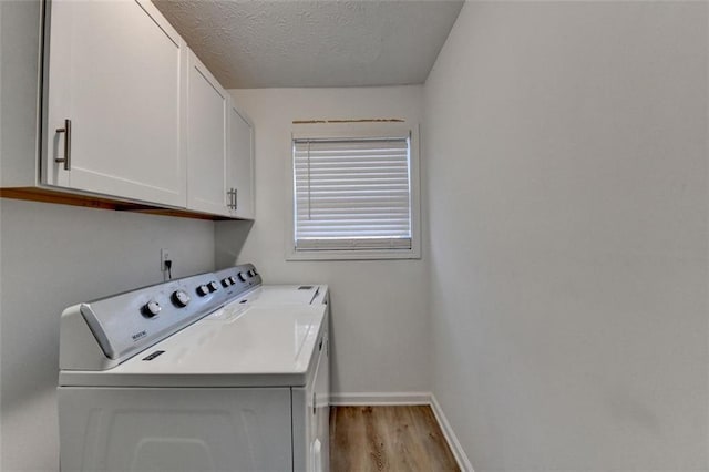 laundry room with cabinets, a textured ceiling, washing machine and clothes dryer, and light hardwood / wood-style floors