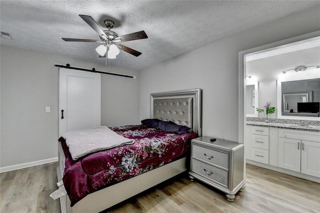 bedroom featuring ensuite bathroom, light hardwood / wood-style flooring, a textured ceiling, ceiling fan, and a barn door