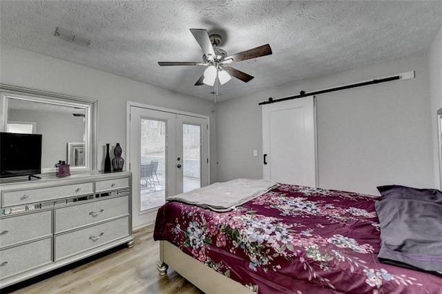 bedroom featuring access to exterior, light hardwood / wood-style floors, a textured ceiling, a barn door, and french doors