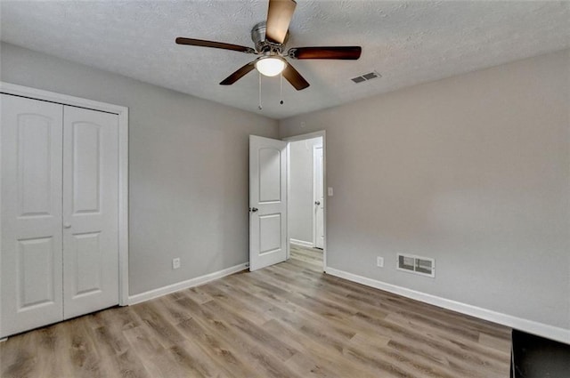 unfurnished bedroom featuring ceiling fan, a closet, light hardwood / wood-style flooring, and a textured ceiling