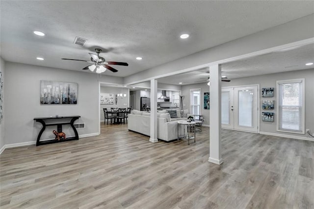 living room featuring ceiling fan, light hardwood / wood-style flooring, and a textured ceiling