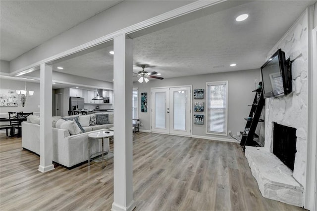 living room with a fireplace, light wood-type flooring, ceiling fan, a textured ceiling, and french doors