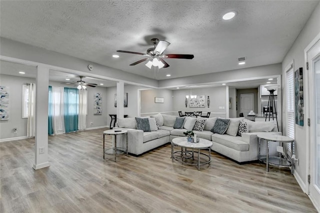 living room with ceiling fan with notable chandelier, a textured ceiling, and light hardwood / wood-style floors