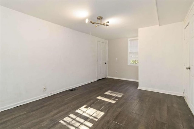 spare room with a notable chandelier and dark hardwood / wood-style floors