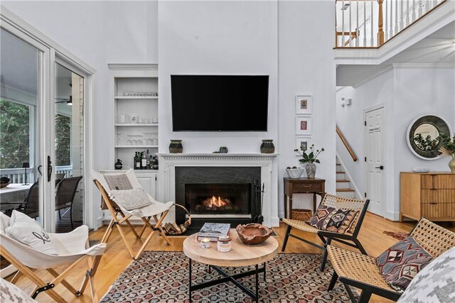 living room with light wood-type flooring, built in shelves, a fireplace, and a high ceiling