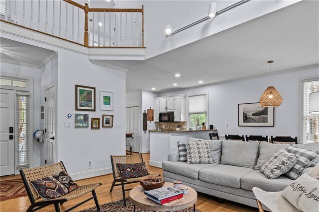 living room featuring light wood-type flooring, plenty of natural light, ornamental molding, and a high ceiling