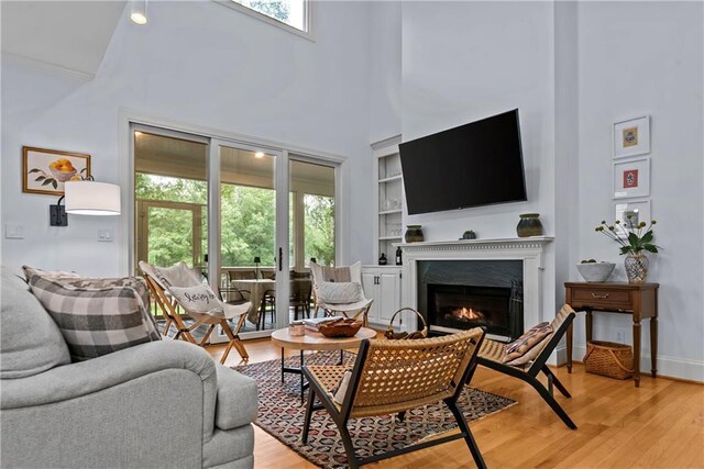 living room with a high end fireplace, a towering ceiling, light hardwood / wood-style flooring, and built in features