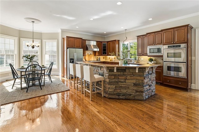 kitchen with appliances with stainless steel finishes, backsplash, a kitchen bar, hardwood / wood-style flooring, and wall chimney exhaust hood