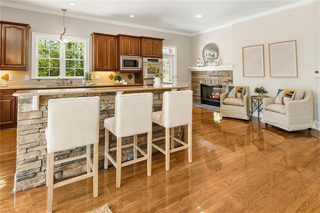 kitchen featuring a kitchen breakfast bar, backsplash, stainless steel appliances, wood-type flooring, and a stone fireplace